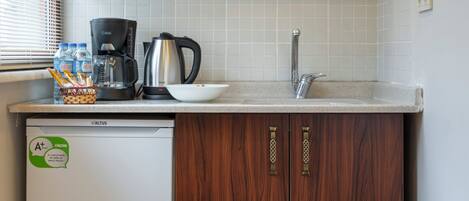 A compact kitchen with wooden cabinets, a microwave, a coffee maker, and a refrigerator.