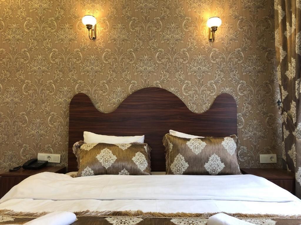 A hotel room with a large bed, two wall-mounted lamps, and a patterned wallpaper.