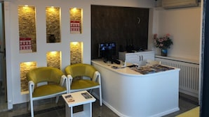 A reception area with a desk, two chairs, a small table with magazines, and a wall with illuminated panels. - Capricorn by Otantik Suites (Istanbul)