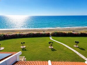 A stunning, high-angle viewpoint showcasing the property’s expansive beachfront frontage and beautifully manicured lawn.
