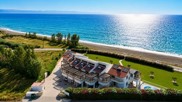 A coastal hotel with multiple balconies, a swimming pool, and a view of the sea.
