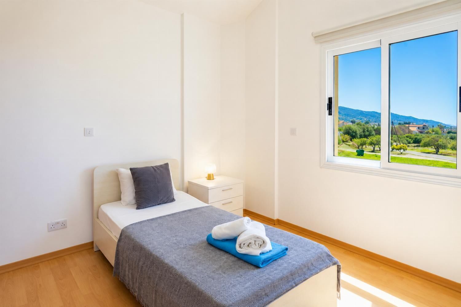 Ein Schlafzimmer mit Bett, Nachttisch und Fenster mit Blick auf Grünflächen und Hügel.