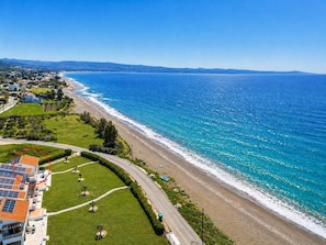 Vista aérea de una zona costera con playa, una carretera que serpentea por la costa y un edificio con paneles solares.