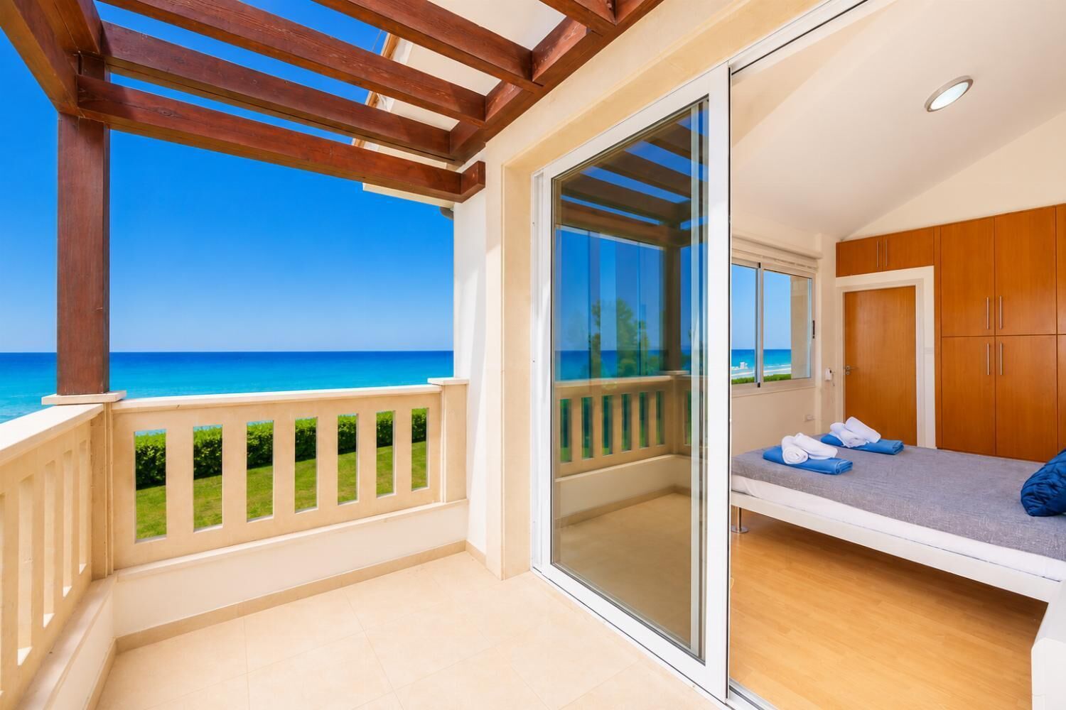 A balcony with a view of the sea, a sliding glass door leading to a bedroom with a bed and a wardrobe.