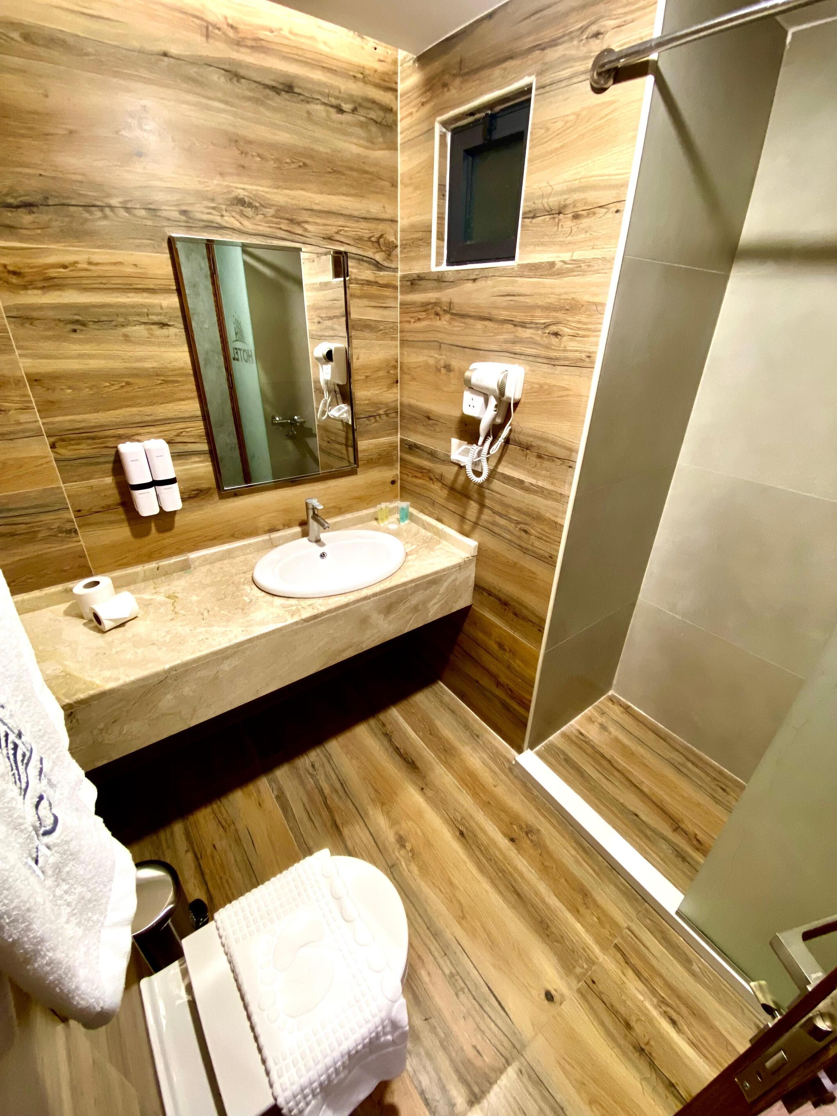 A modern bathroom with a wooden wall, a sink, a mirror, a towel, and a shower area.