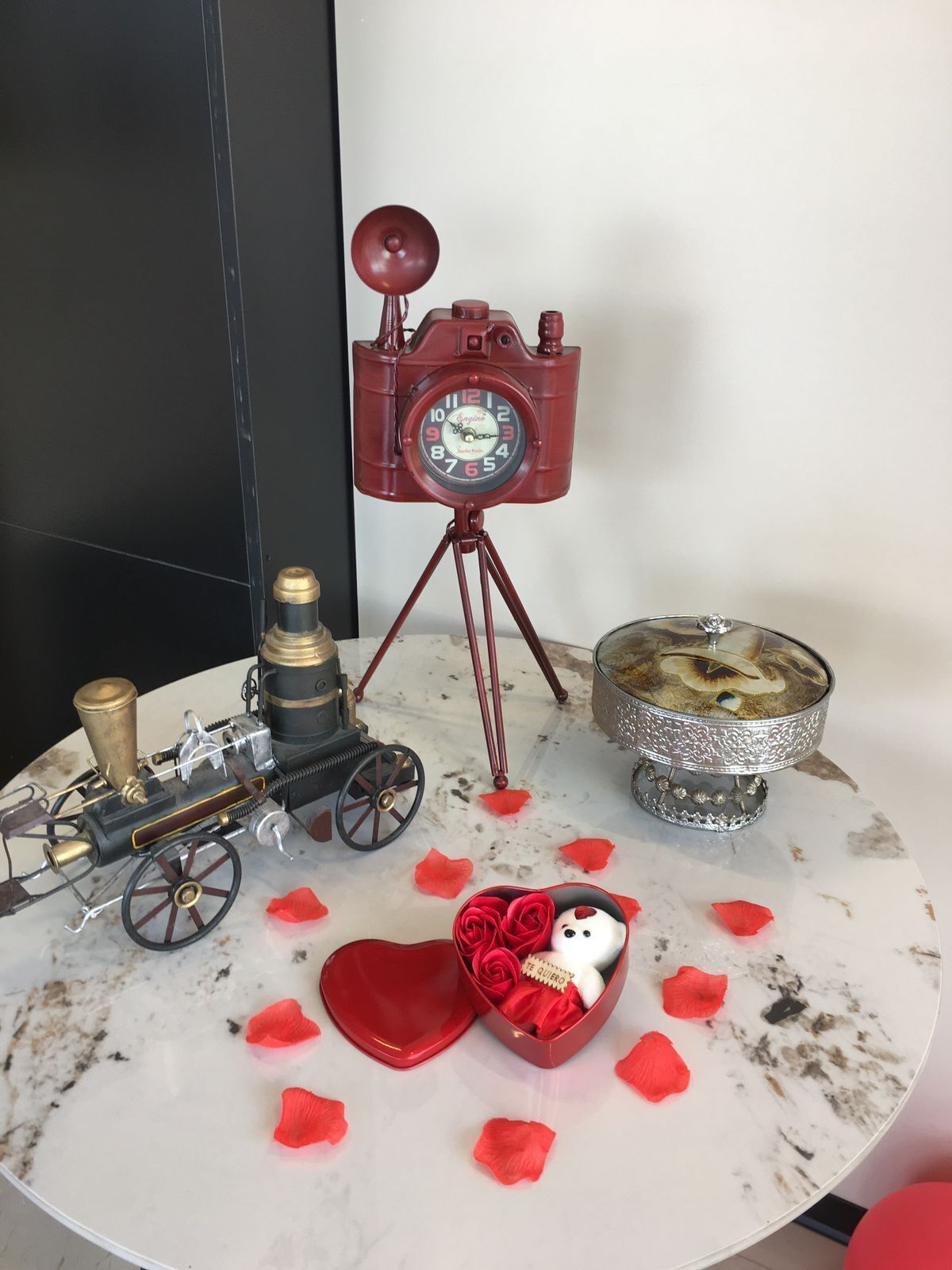 A table with a vintage train model, a red clock, and a decorative silver bowl.