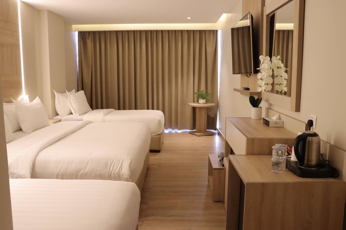 A hotel room with two beds, a small round table with a plant, a coffee maker, and a TV mounted on the wall.