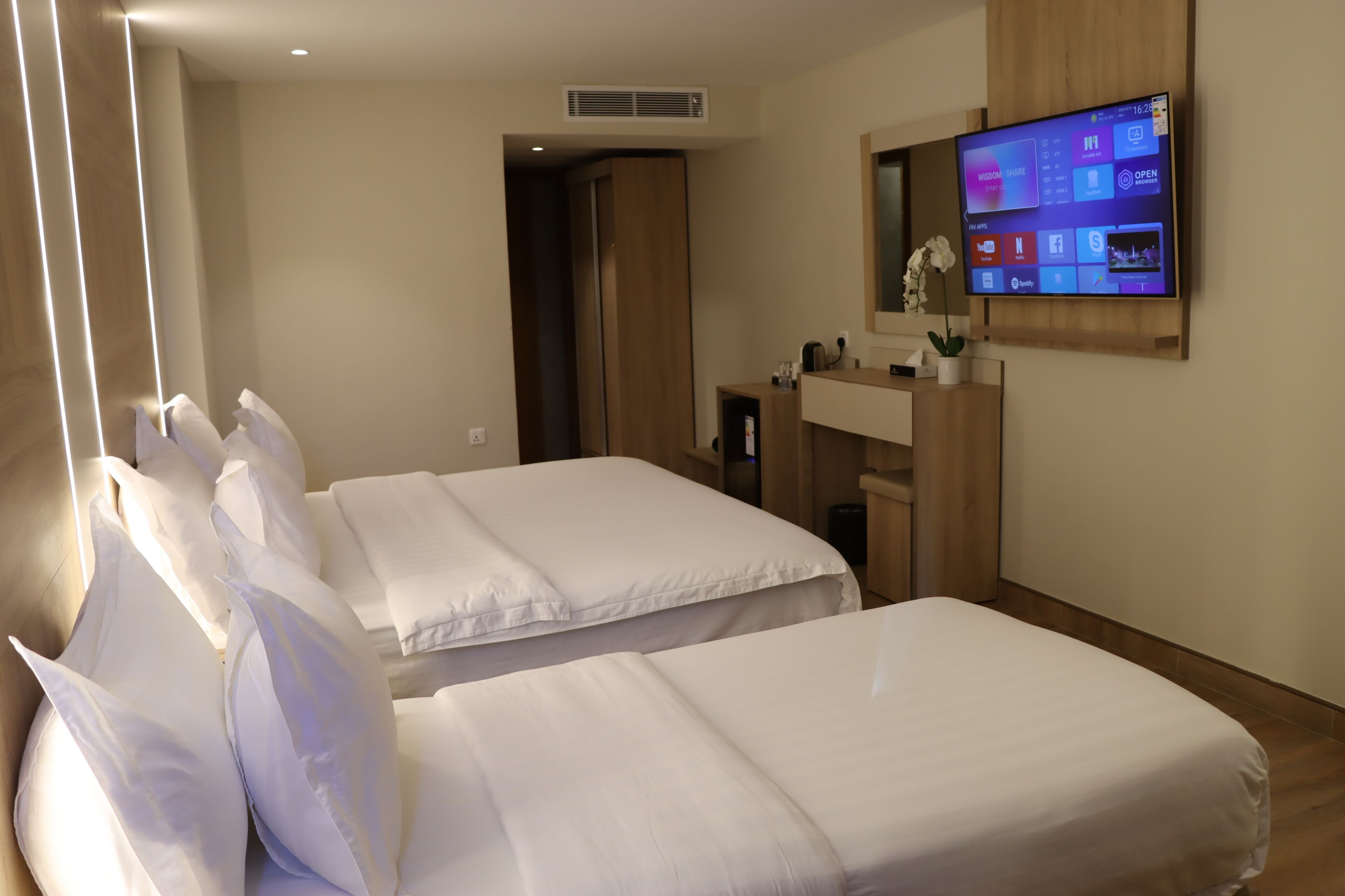 A hotel room with two beds, a TV mounted on the wall, and a wooden cabinet.