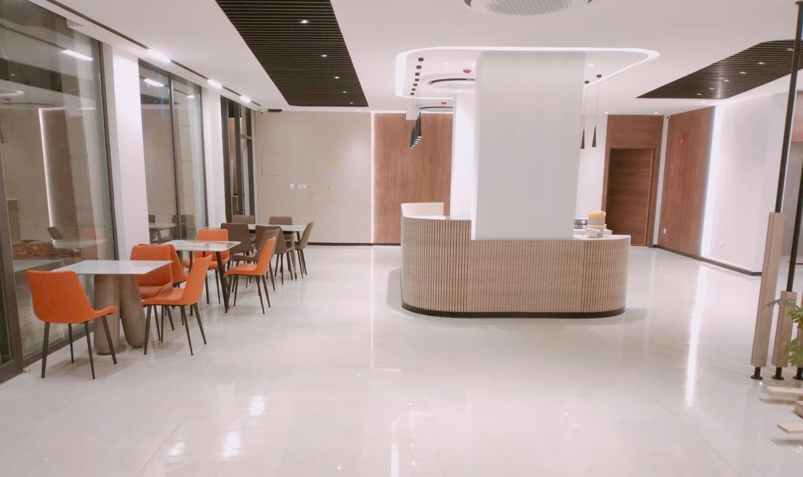 A modern reception area with a central desk, glass walls, and orange chairs.