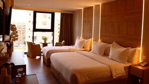 Camera d'albergo con due letti, una scrivania, una sedia, una televisione e una finestra che si affaccia su edifici.