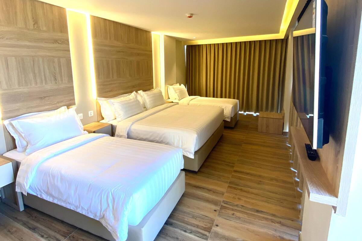 A hotel room with two beds, wooden flooring, a flat-screen TV, and a large window with curtains.