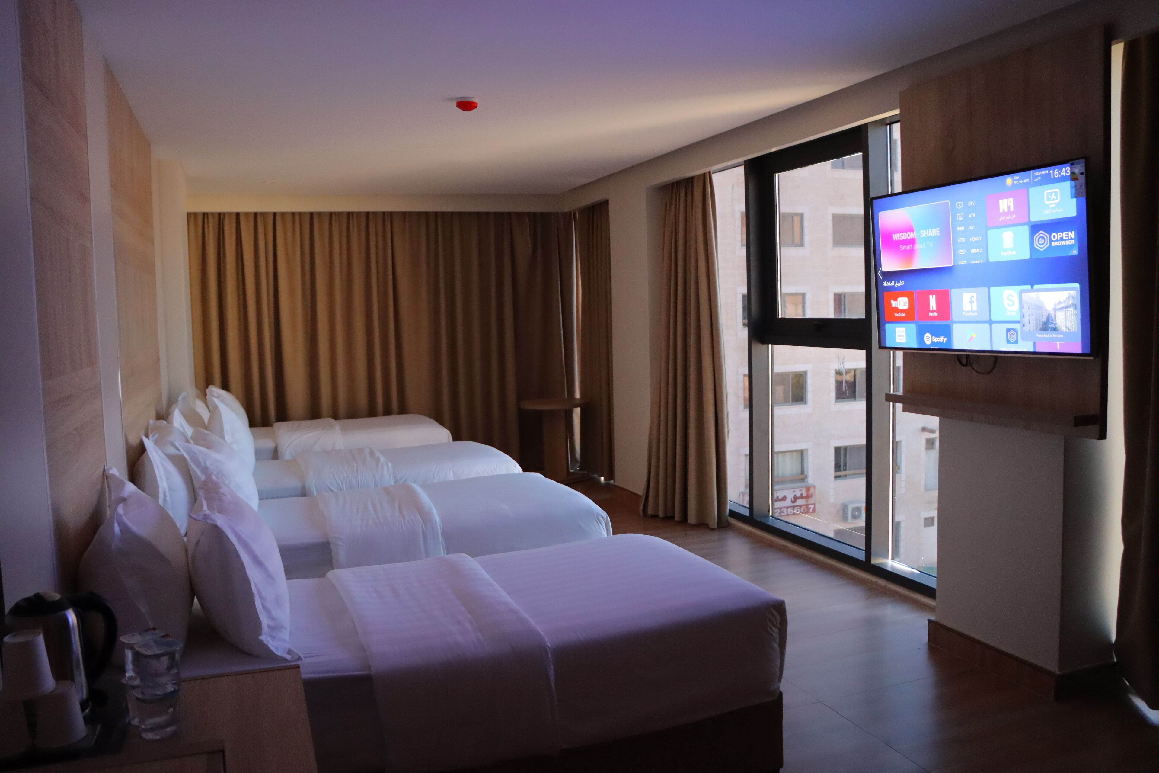 A hotel room with two beds, a TV on the wall, and a large window.