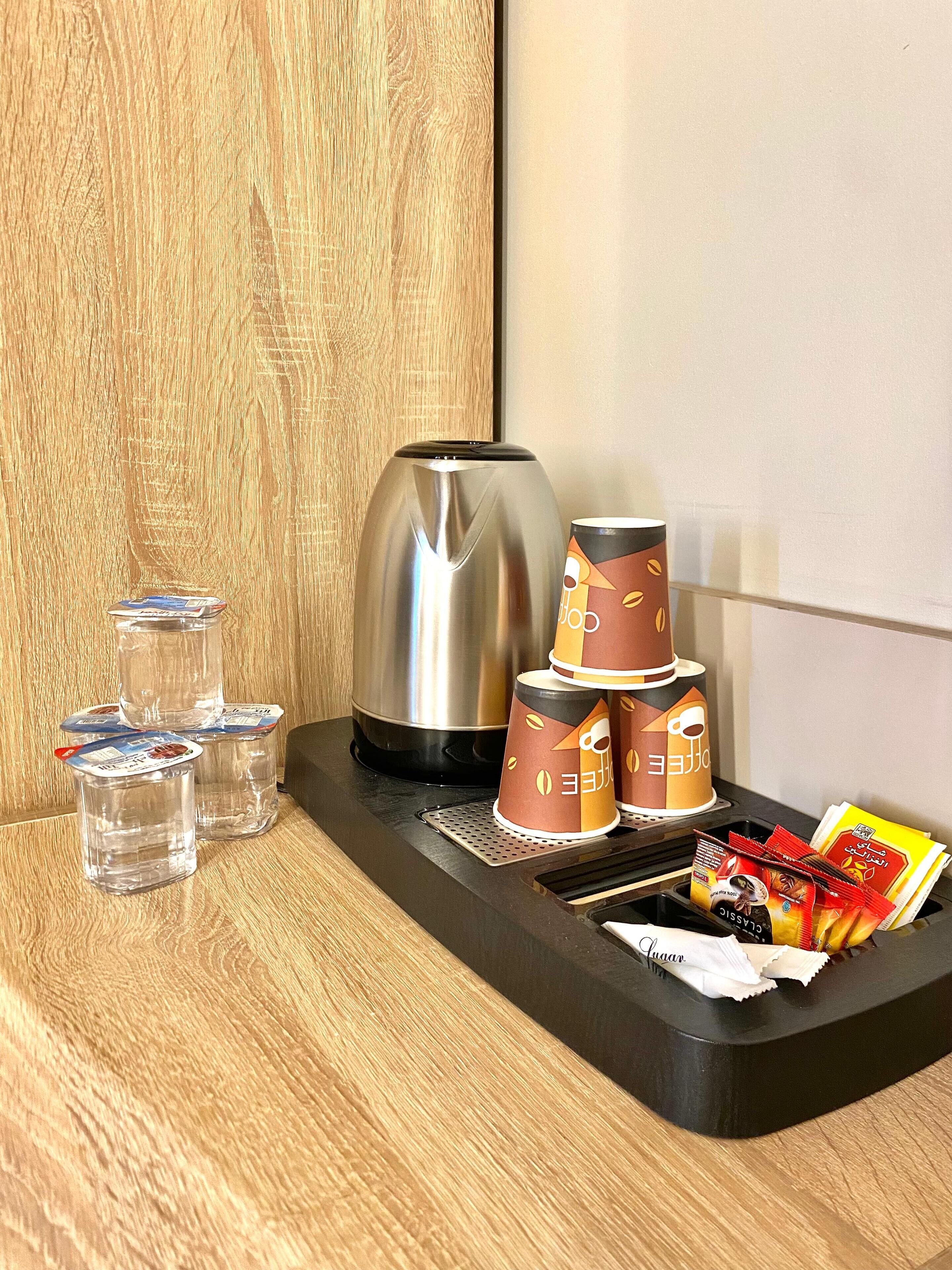 De minibar van een hotelkamer, met een koffiezetapparaat, waterflesjes, wegwerpbekers en koffiepads.
