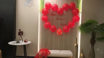 A room with a heart-shaped balloon decoration, a bench, a table with a camera, and a plant.