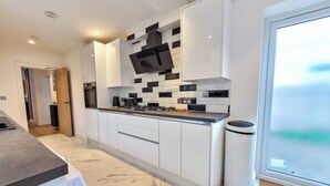 A modern kitchen with white cabinets, a black and white backsplash, and a built-in oven. - 4 bed 2 bath spacious lovely house in Ilford London (Ilford)
