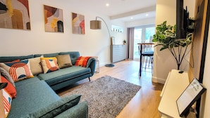 A modern living room with a teal sofa, a small rug, and abstract wall art. - 4 bed 2 bath spacious lovely house in Ilford London (Ilford)