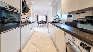 A modern kitchen with a central island, built-in appliances, and a dining area with a view to the living room. - 4 bed 2 bath spacious lovely house in Ilford London (Ilford)