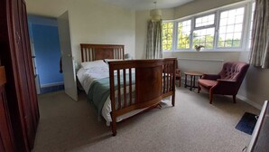 A bedroom with a wooden bed, a chair, a small table, and a window with curtains. - Private 1-bedroom apartment in Raynes Park (London)