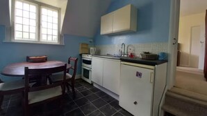 A compact kitchen with a dining table, chairs, a stove, a sink, and cabinets. - Private 1-bedroom apartment in Raynes Park (London)