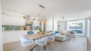 Una cocina moderna con armarios blancos, una mesa de comedor de madera y lámparas colgantes.