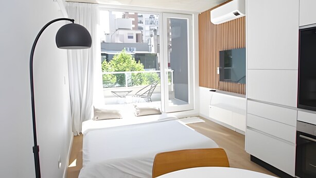 A modern bedroom with a bed, a desk, and a balcony with a view of buildings and trees. - 801 O "Your Temporary Home (Ciudad Autónoma de Buenos Aires)