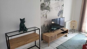 Ein modernes Wohnzimmer mit einem Holz-TV-Schrank, einem Glastisch und einer dekorativen Katzenfigur.
