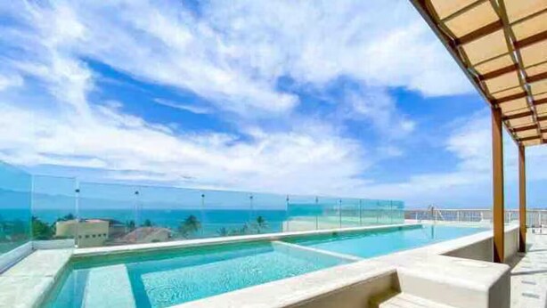A rooftop infinity pool with clear blue water, a glass barrier, and a view of the ocean.