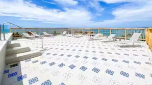 A rooftop terrace with sun loungers and a patterned floor, overlooking a body of water.