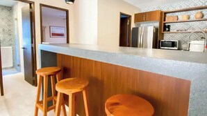 A modern kitchen with a central island, wooden stools, pendant lighting, and built-in appliances.