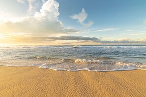 Ein Strand mit sanft anschwellenden Wellen unter einem teils bewölkten Himmel.