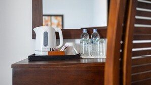 Une chambre d’hôtel avec une petite table en bois sur laquelle se trouvent une bouilloire électrique blanche, un plateau avec des stylos et des crayons, et deux bouteilles d’eau en verre.