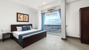 Une chambre à coucher avec un grand lit, une table de chevet, un climatiseur fixé au mur et une fenêtre avec des rideaux.