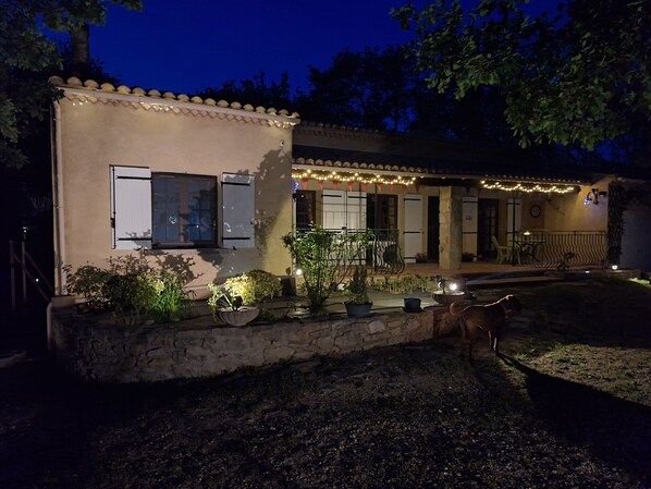 A building with a stone foundation, a balcony with plants, and string lights.
