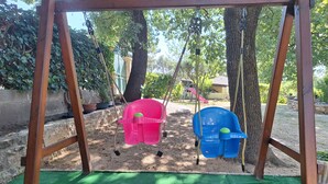 A swing set with two swings, a green artificial turf ground, and a background with trees and a building. - THE PROVENCE (Bollène)