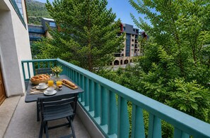 Un balcon avec une table dressée pour le petit-déjeuner, donnant sur un espace verdoyant luxuriant et un bâtiment au design architectural unique.