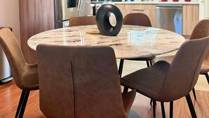A modern kitchen with wooden cabinets, a stainless steel refrigerator, and a dining area with a marble table and leather chairs.