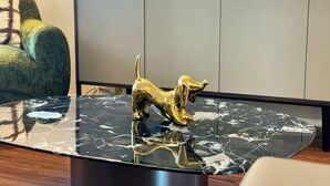 A modern living room with a marble coffee table, a golden dog sculpture, a television, and a green armchair.