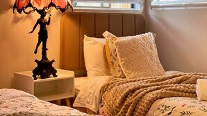 A bedroom with a bed, a nightstand, a lamp, and two windows with blinds.