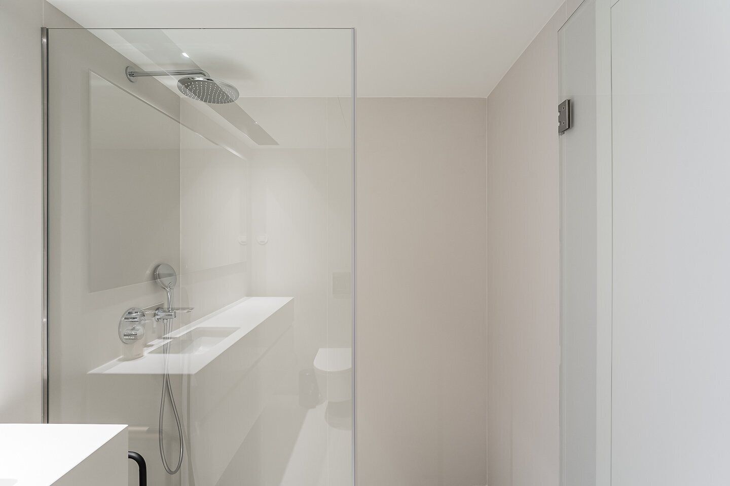 Una dutxa moderna amb envàs de vidre, un lavabo blanc i un braç de dutxa manual.