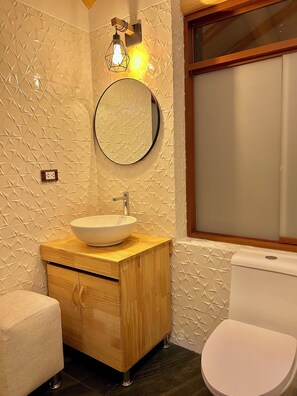 Ein Badezimmer mit einem runden Spiegel, einem Holzwaschtisch, einem weißen Waschbecken und einer Toilette.