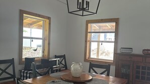 Un comedor con una mesa de madera, sillas negras, una lámpara colgante y dos ventanas con marcos de madera.