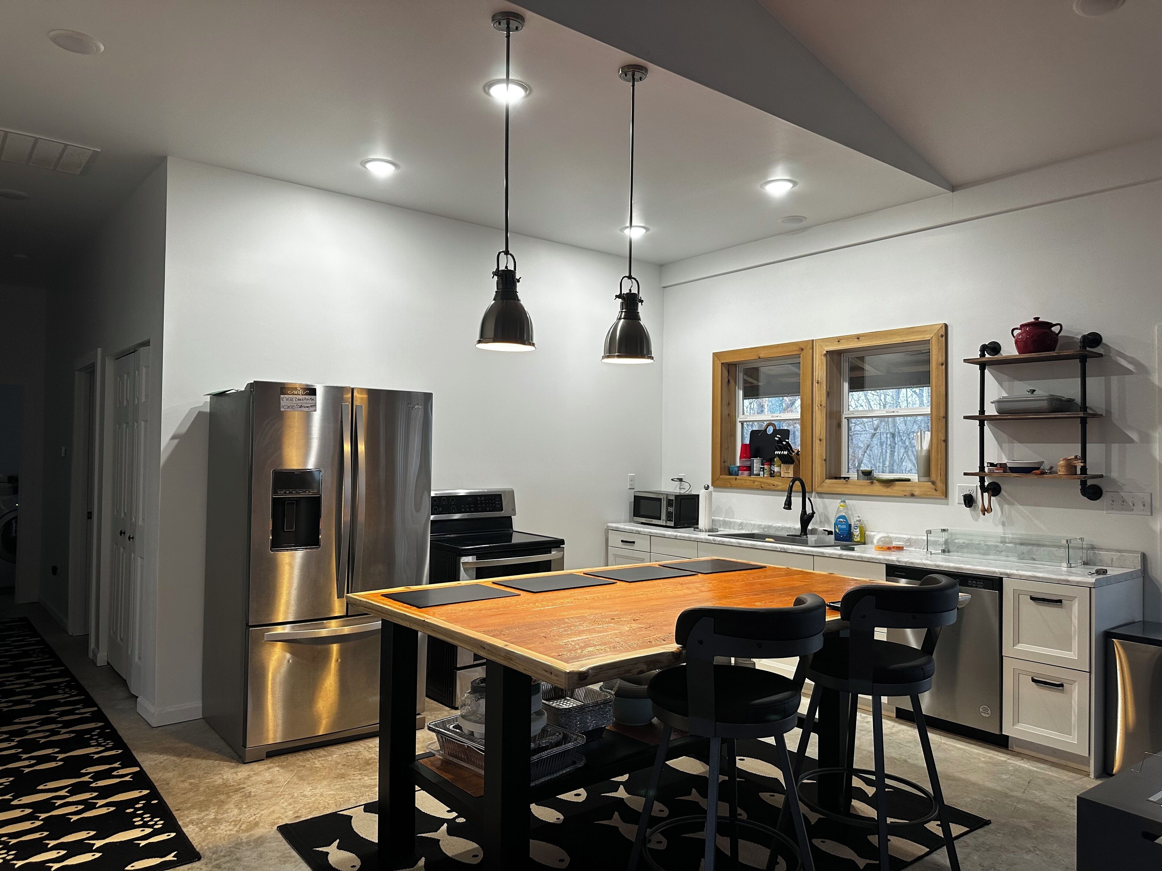 Une cuisine moderne dotée d’appareils électroménagers en acier inoxydable, d’une table à manger en bois, de chaises noires et de luminaires suspendus.