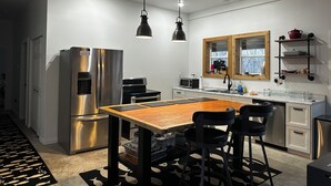 Una cocina moderna con electrodomésticos de acero inoxidable, una mesa de comedor de madera, sillas negras y luces colgantes.