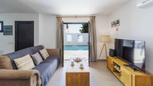 A modern living room with a sofa, a coffee table, a TV, and a view of a swimming pool. - Villa Sol - Two Bedroom Villa, Sleeps 4 (Puerto del Carmen)