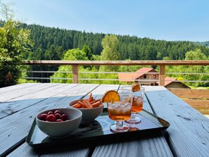 A wooden table with a tray containing glasses of amber-colored beverage, bowls of raspberries, and orange slices. - Chalet Les Cimes - Sauna - Jacuzzi (Gérardmer)