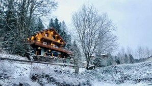 A wooden lodge with a balcony overlooking a snow-covered landscape and a river.