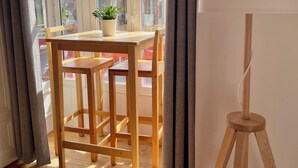 Een kamer met een houten tafel en stoelen, een kamerplant en een driepootlamp.