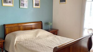 Een slaapkamer met een houten bed, een nachtkastje, een lamp en drie ingelijste foto's aan de muur.