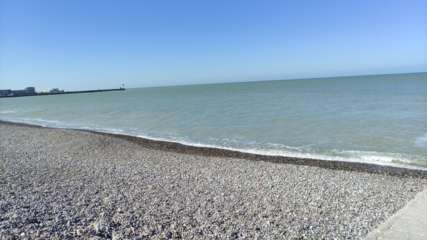 Een kiezelstrand met een heldere lucht en kalme zee.