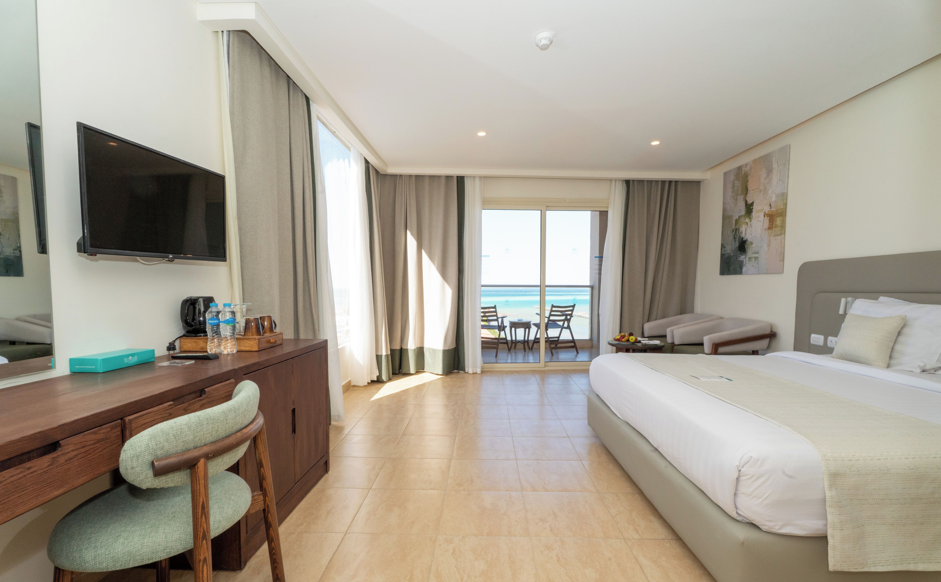 Une chambre d’hôtel équipée d’un lit, d’un bureau, d’une chaise, d’une télévision et offrant une vue sur la mer.